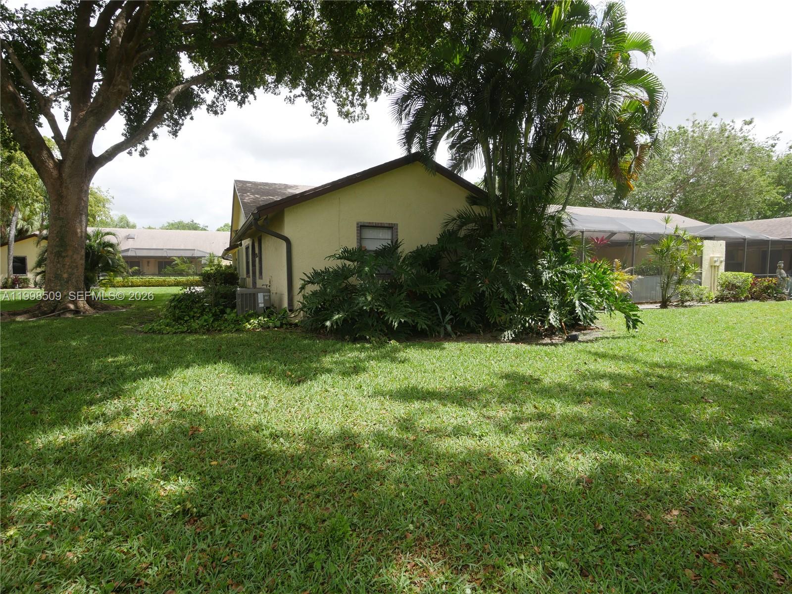 A yellow house with a screened-in patio sits on a grassy lawn with trees — 23359 Barlake Dr, Boca Raton FL 33433, BOCA RATON, FL
