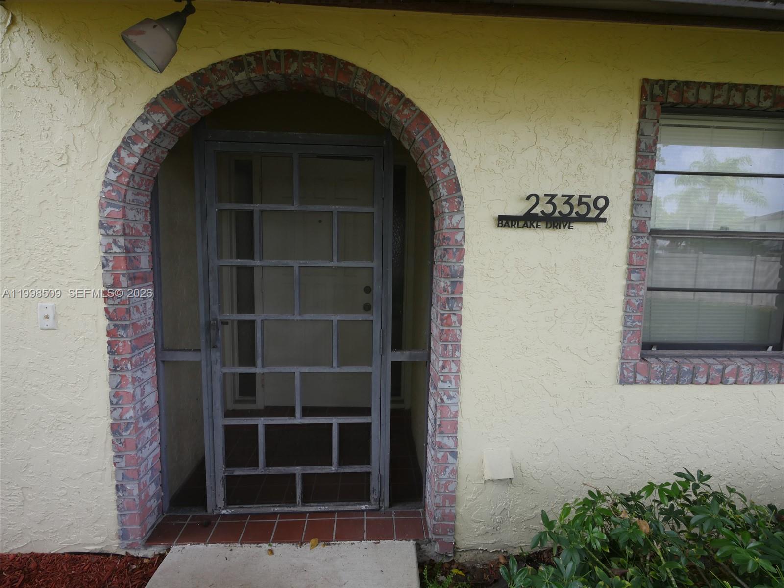 An arched brick entryway leads to a metal screen door on a stucco house — 23359 Barlake Dr, Boca Raton FL 33433, BOCA RATON, FL