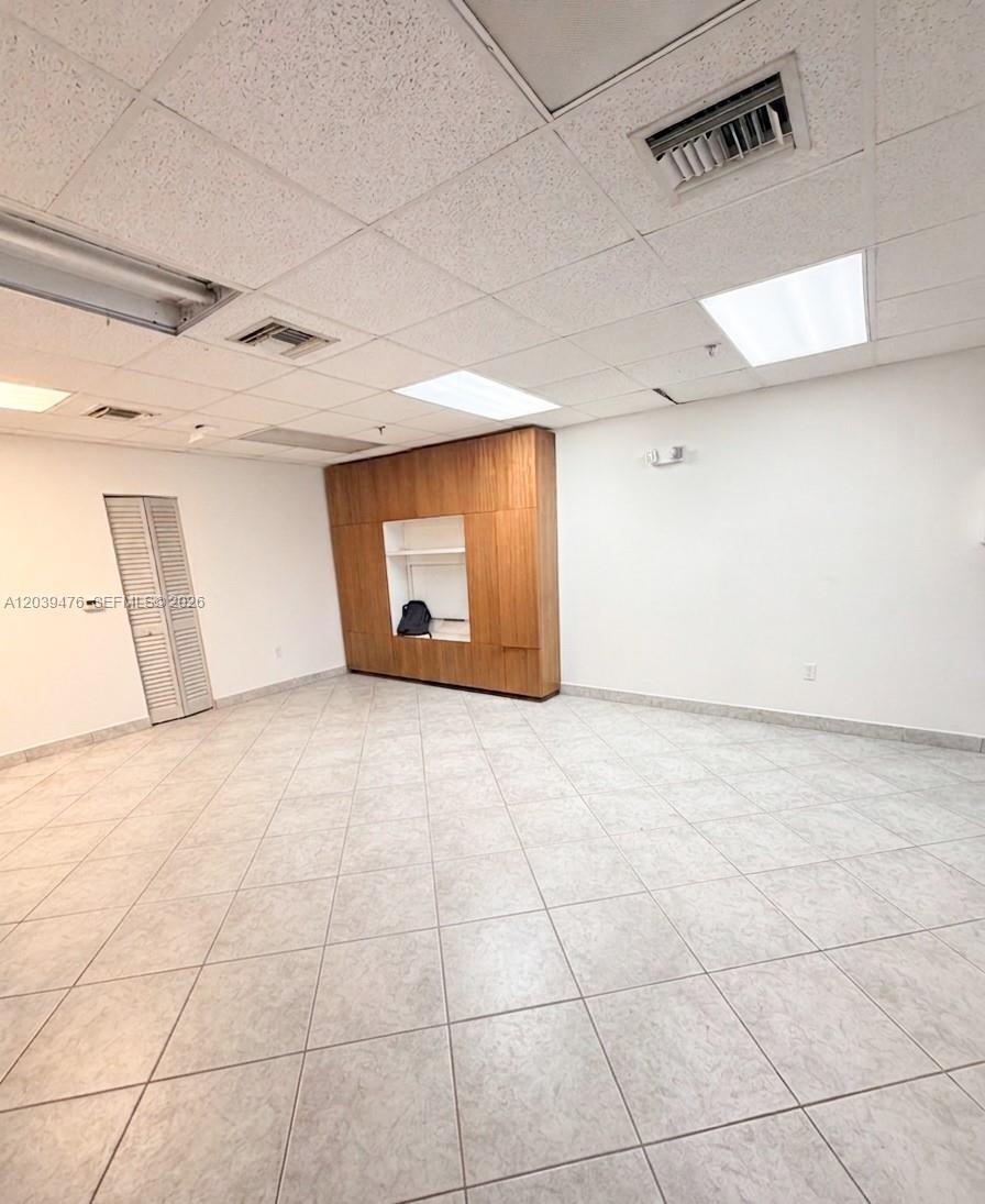 An empty office room features light-colored tile flooring, a drop ceiling, and built-in wooden cabinetry — 8554 NW 61st St, Miami FL 33166, MIAMI, FL