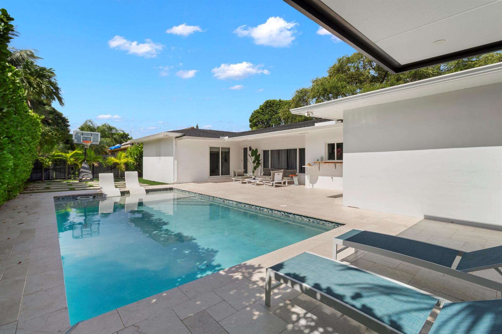 A backyard features a swimming pool, lounge chairs, a basketball hoop, and a white house — 21303 NE 18th Place, Miami FL 33179, MIAMI, FL