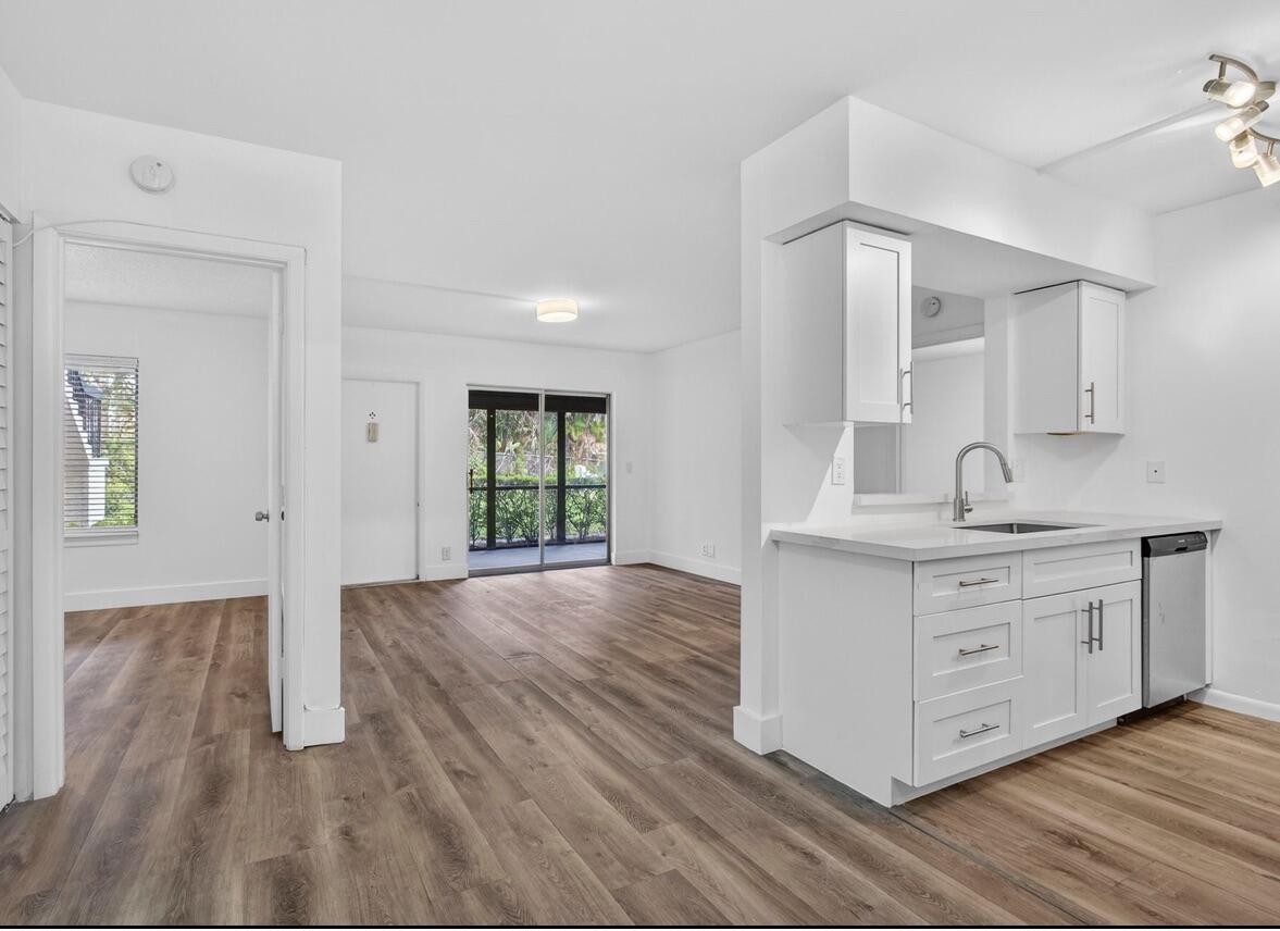 A white kitchen with quartz countertops overlooks a living area with wood-look flooring — 6258 Chasewood Drive # C, Jupiter FL 33458, JUPITER, FL