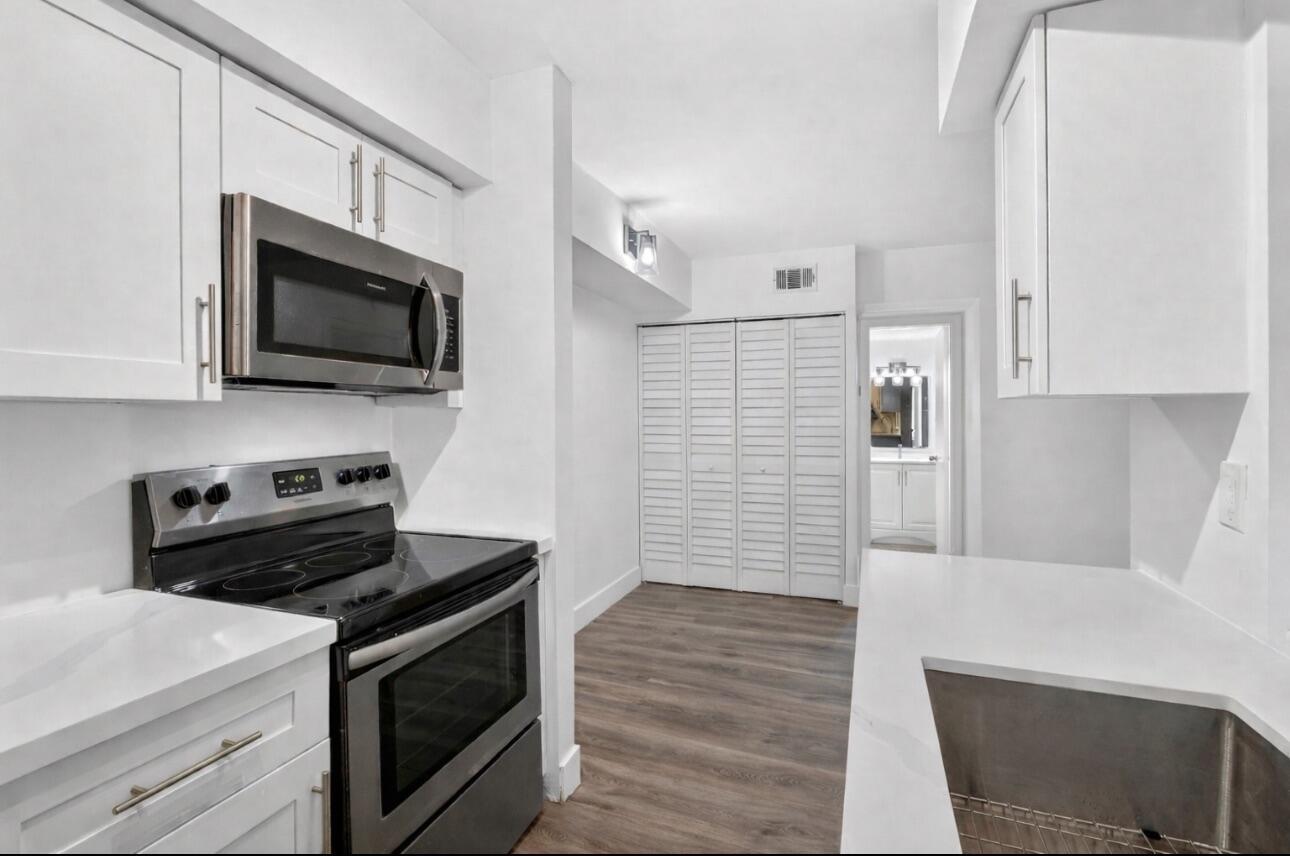 A modern kitchen features white cabinets, stainless steel appliances, and white countertops — 6258 Chasewood Drive # C, Jupiter FL 33458, JUPITER, FL