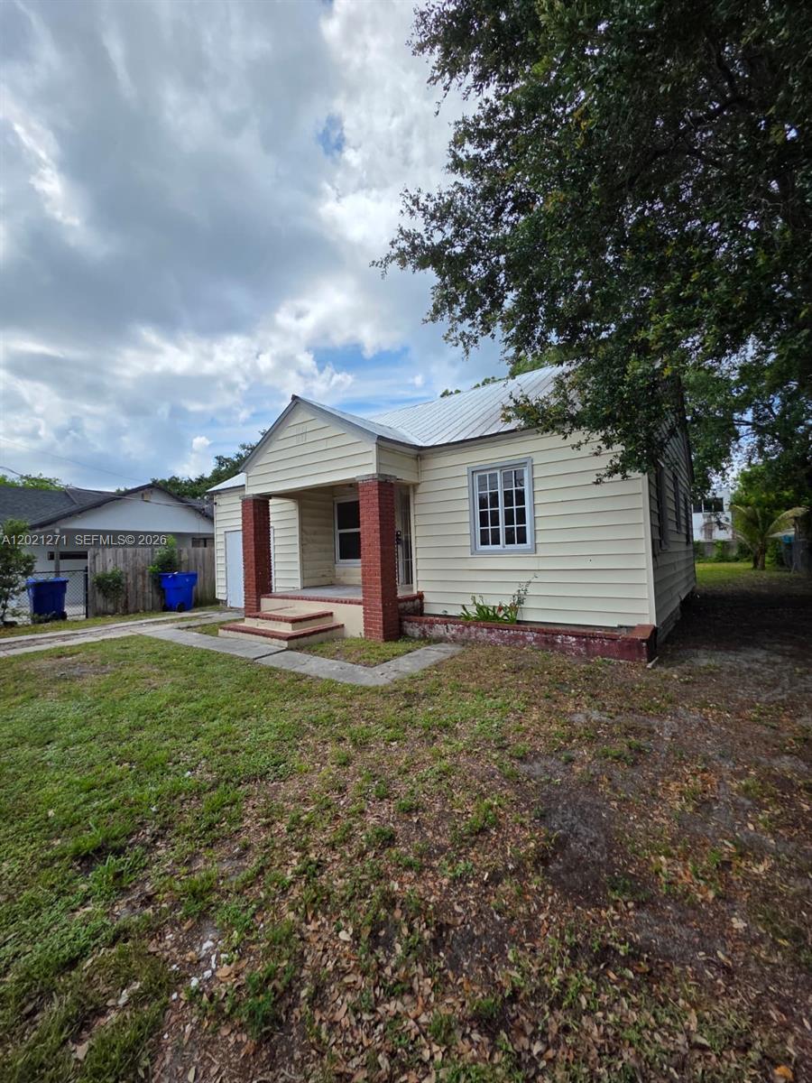 A single-story house with light-colored siding, a metal roof, and a brick-columned front porch — 315 NW 53rd St # 0, Miami FL 33127, MIAMI, FL
