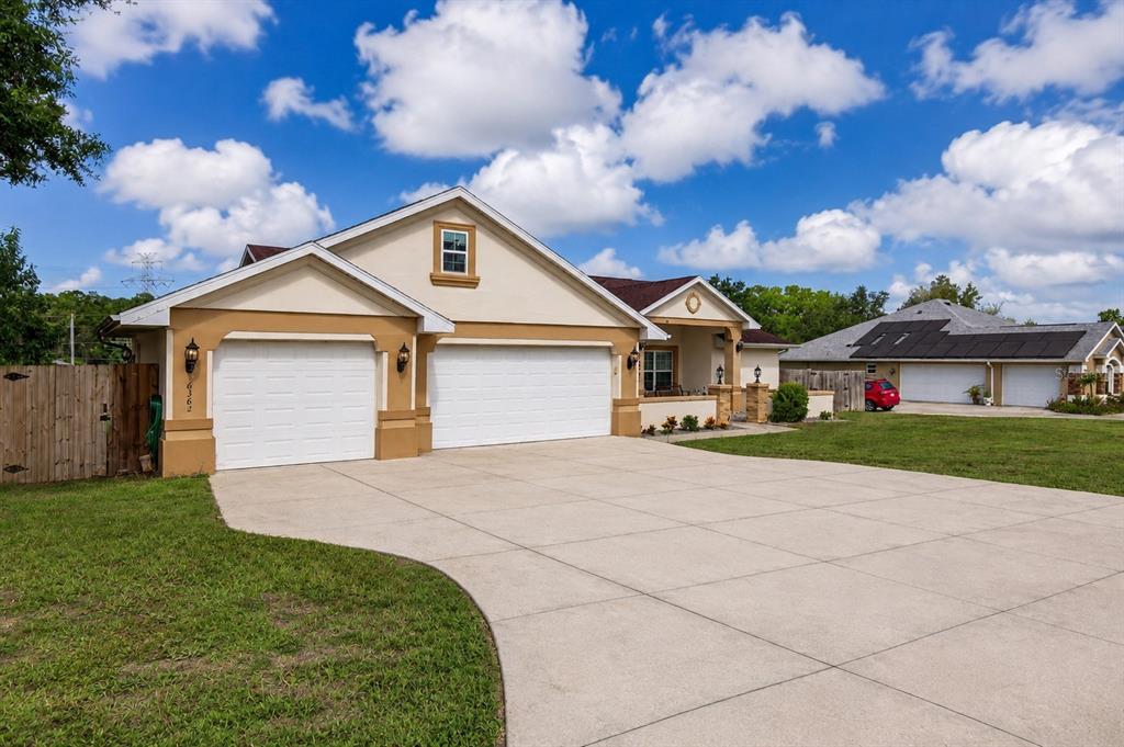 A tan house with a three-car garage and a concrete driveway under a cloudy sky — 16362 SE 81ST TERRACE, SUMMERFIELD, FL