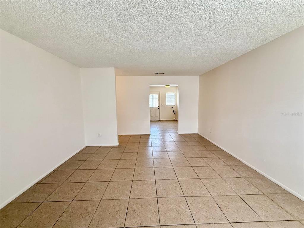 An empty room with beige tile flooring and white walls leads to a rear doorway — 3107 W MARCUM STREET UNIT A, TAMPA, FL