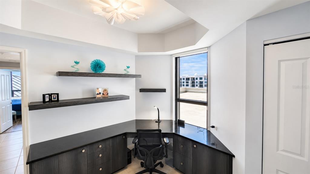 A home office features a built-in corner desk, dark cabinetry, floating shelves, and a window — 50 CENTRAL AVENUE UNIT 11A, SARASOTA, FL