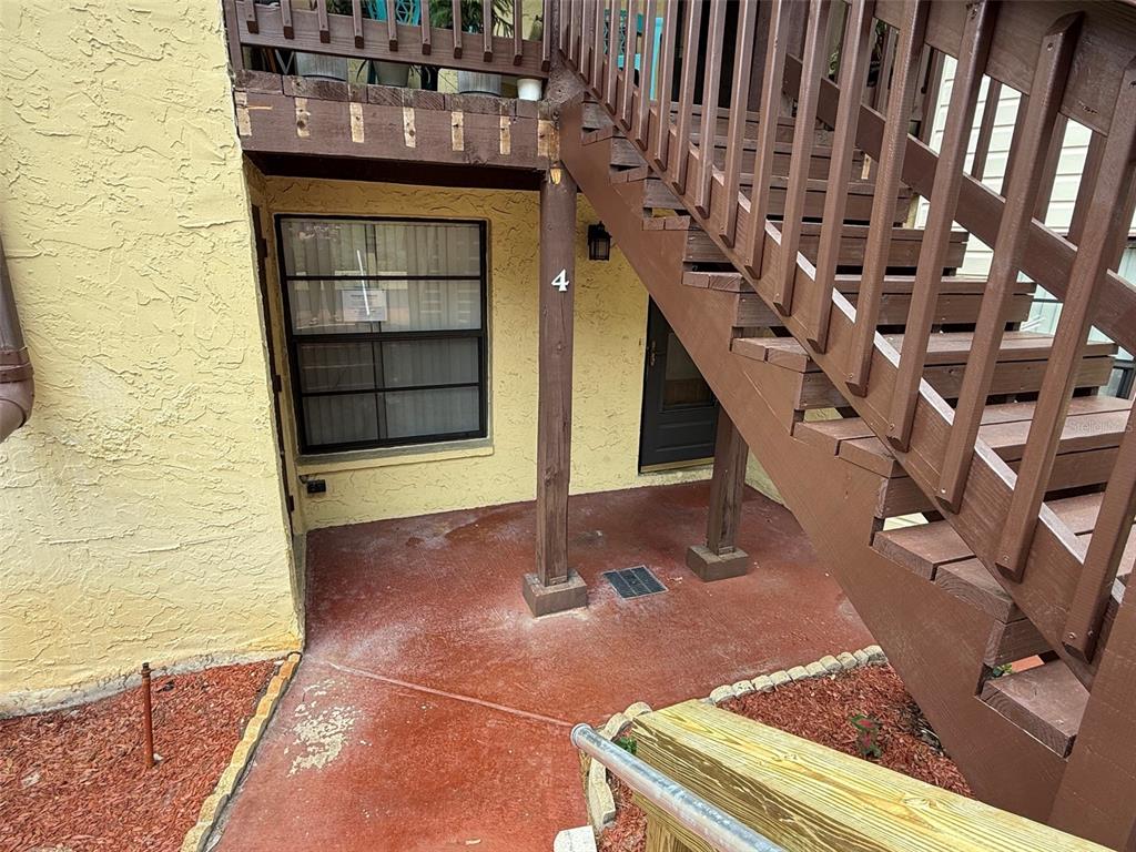 A ground-level patio area features a window, a dark door, and wooden stairs overhead — 8621 SHADBLOW COURT UNIT 4, PORT RICHEY, FL