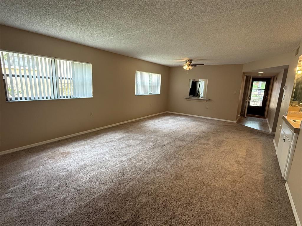 An empty living room features beige carpet, tan walls, vertical blinds, and a ceiling fan — 8621 SHADBLOW COURT UNIT 4, PORT RICHEY, FL