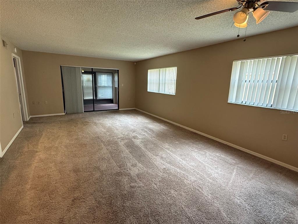 An empty living room features beige carpet, tan walls, a ceiling fan, and vertical blinds — 8621 SHADBLOW COURT UNIT 4, PORT RICHEY, FL