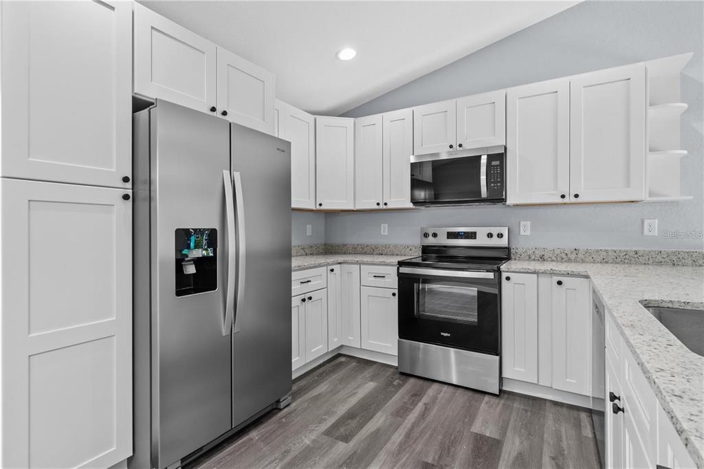 A kitchen features white cabinets, stainless steel appliances, and speckled granite countertops — 14845 SW 77TH AVENUE, OCALA, FL