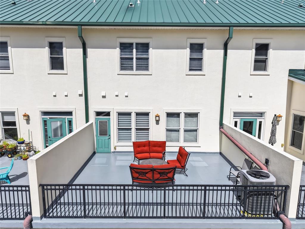 An elevated outdoor patio features red furniture, a metal railing, and a light-colored building exterior — 125 NE 4TH STREET UNIT 38, GAINESVILLE, FL