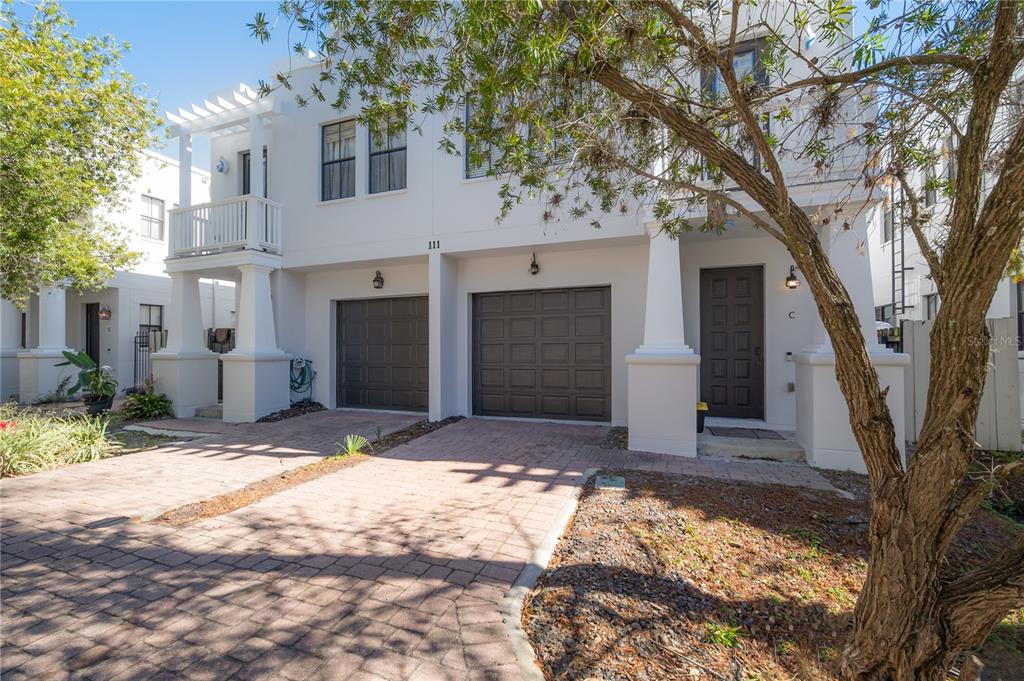 A two-story white townhouse features two garage doors, a front entrance, and a brick driveway — 111 S PACKWOOD AVENUE UNIT C, TAMPA, FL