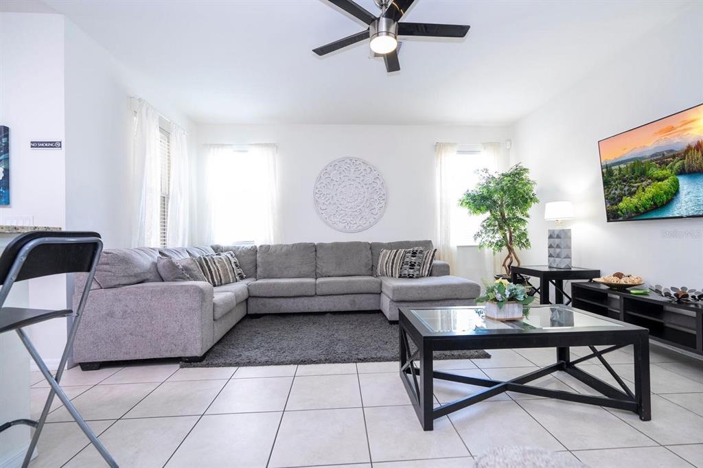 A living room features a gray sectional sofa, a glass-topped coffee table, and tiled floors — 2625 SANTOSH COVE, KISSIMMEE, FL