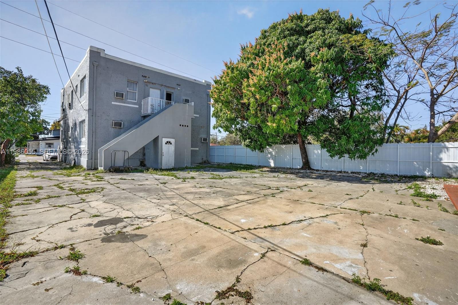 A gray two-story building features an exterior staircase and a large tree in a parking lot — 767 NW 35th St, Miami FL 33127, MIAMI, FL