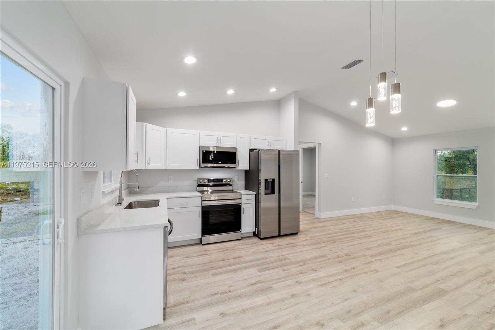 A modern kitchen features white cabinetry, stainless steel appliances, and light wood-look flooring — 15594 SW 38th Place, Ocala FL 33481, OCALA, FL