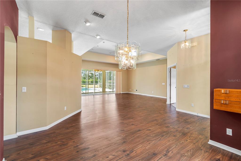 A spacious living area features wood-look flooring, a large crystal chandelier, and sliding glass doors — 5334 LEGEND HILLS LANE, SPRING HILL, FL