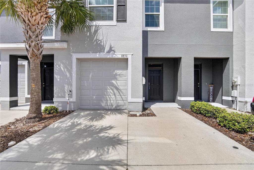 A two-story townhouse exterior features a single-car garage, a palm tree, and two entry doors — 8850 INDIGO TRAIL LOOP, RIVERVIEW, FL