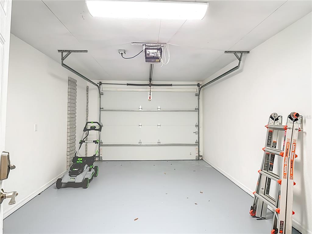A clean, one-car garage with white walls, a gray floor, a lawnmower, and a ladder — 3604 W BAY TO BAY BOULEVARD, TAMPA, FL