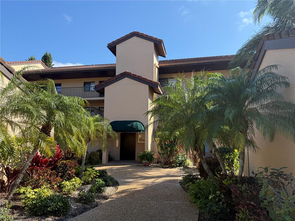 A multi-story tan stucco building with a central entrance and surrounding tropical landscaping — 5525 ASHTON LAKE DRIVE UNIT 5525, SARASOTA, FL
