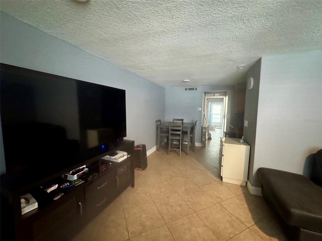 A living room with tile flooring, a large television, and a dining set in back — 4235 SHELDON PLACE UNIT 4235, NEW PORT RICHEY, FL