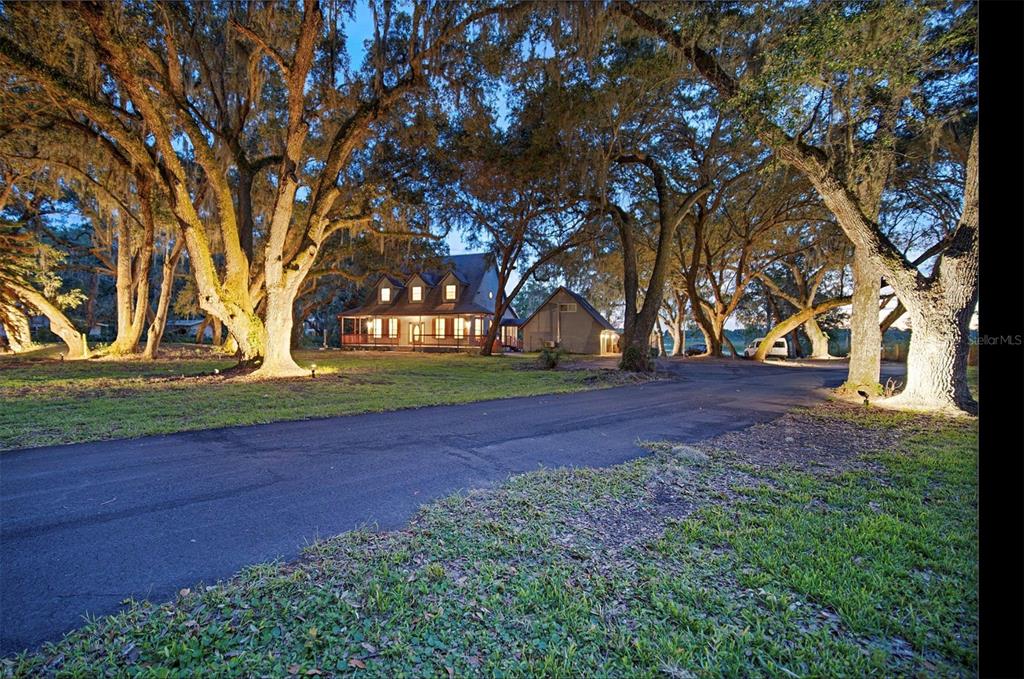 A two-story house with a wrap-around porch sits among large oak trees at dusk — 2890 FRONTIER DRIVE, KISSIMMEE, FL