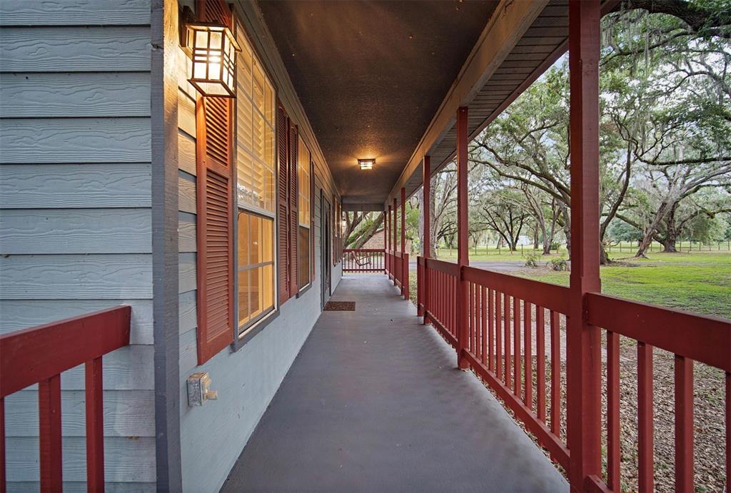 A long, covered porch with red railings and shutters overlooks a grassy yard with trees — 2890 FRONTIER DRIVE, KISSIMMEE, FL
