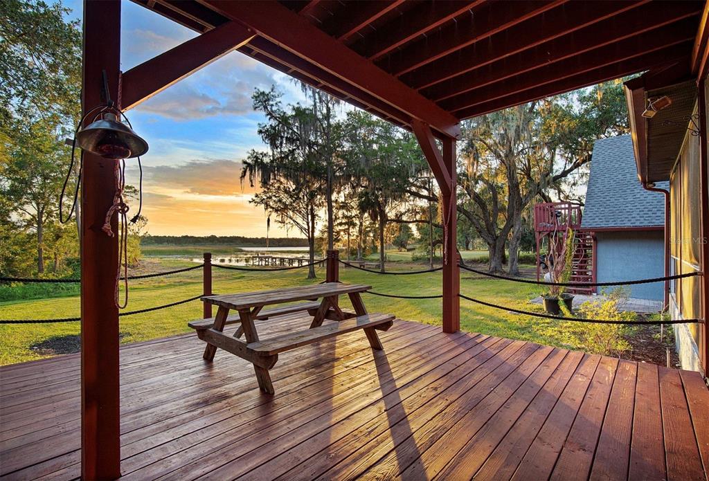 A wooden deck with a picnic table overlooks a grassy yard, trees, and a lake — 2890 FRONTIER DRIVE, KISSIMMEE, FL