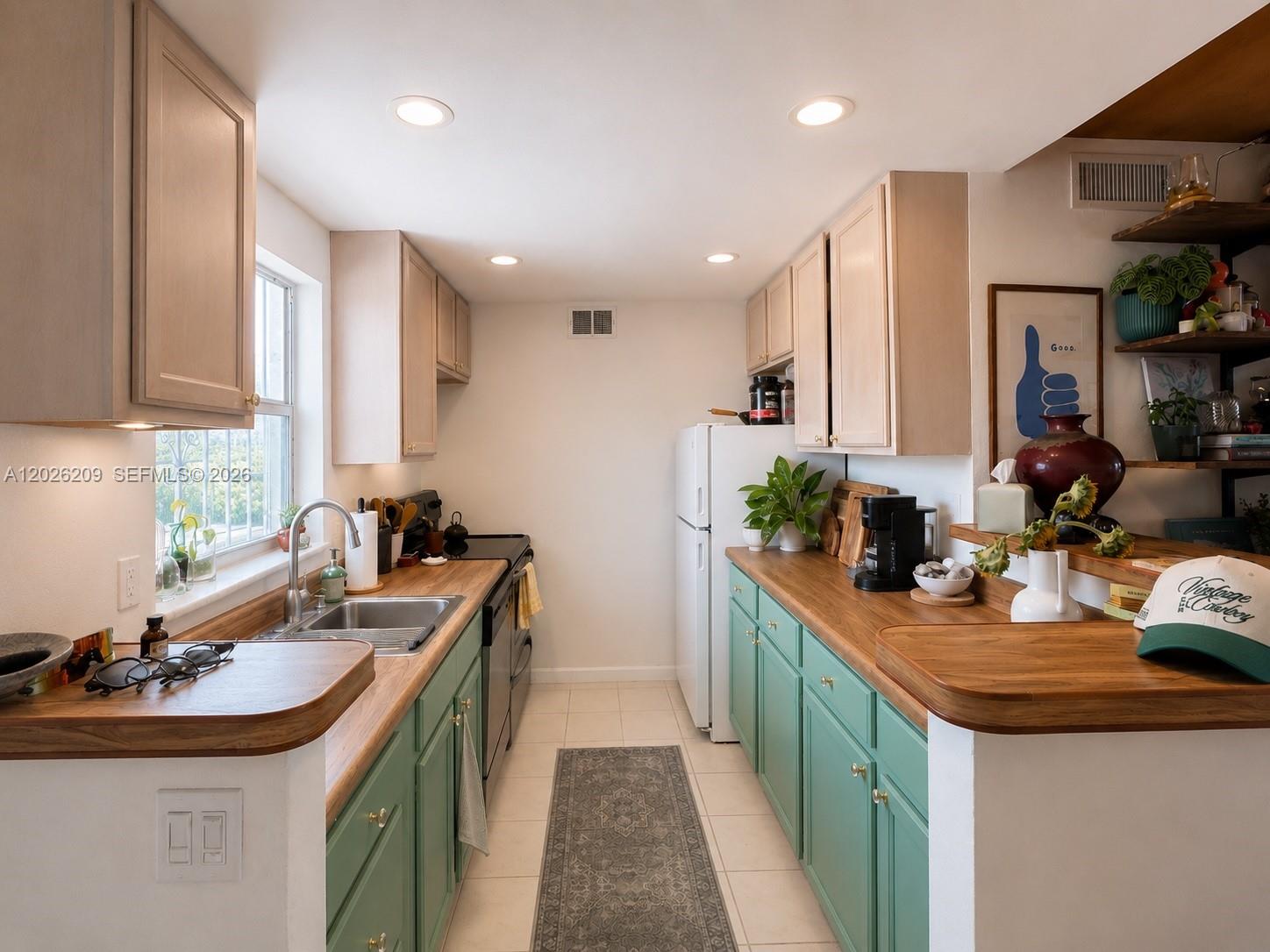 A galley kitchen features green lower cabinets, light wood upper cabinets, and wood countertops — 910 Jefferson Ave # 5C, Miami Beach FL 33139, MIAMI BEACH, FL