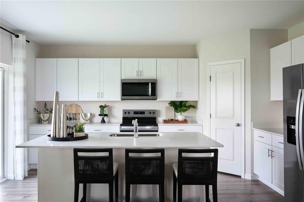 A modern kitchen features white cabinets, a central island with bar seating, and stainless appliances — 1747 VANILLA STREET, HAINES CITY, FL