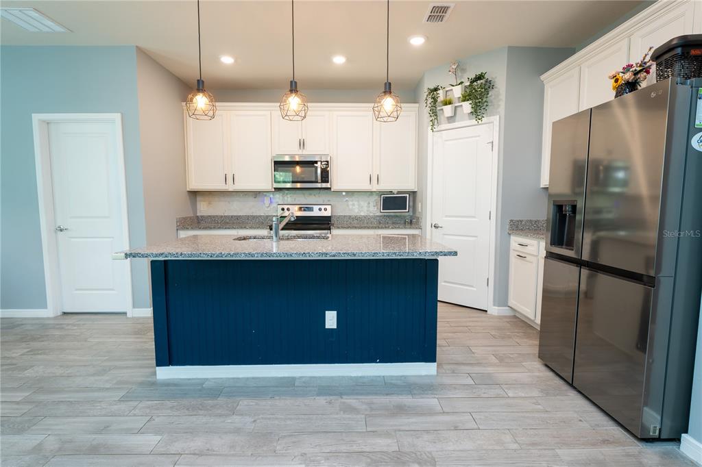 A kitchen features white cabinets, granite countertops, a blue island, and stainless steel appliances — 9683 BROWN BURROW STREET, ORLANDO, FL