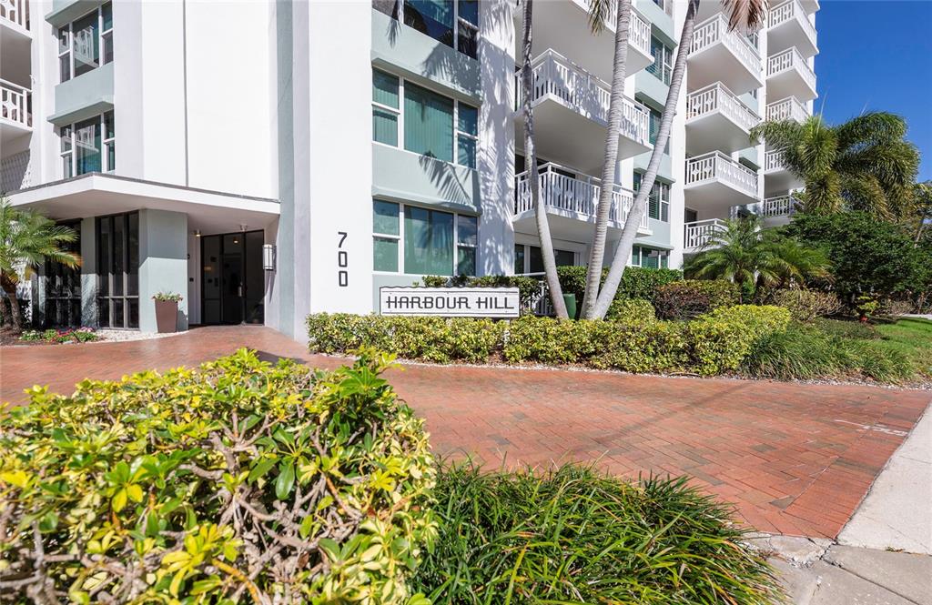 The exterior of a multi-story white apartment building features a brick driveway and landscaping — 700 BEACH DRIVE NE UNIT 406, ST PETERSBURG, FL