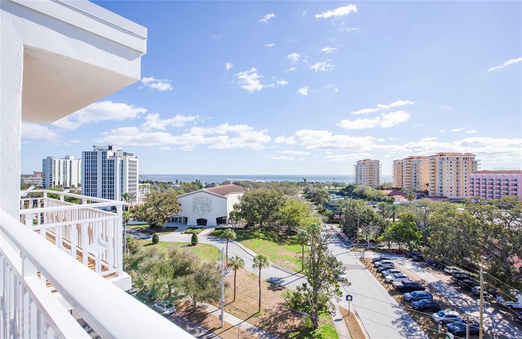 A high-angle view from a balcony overlooking a parking lot, trees, and distant coastal buildings — 700 BEACH DRIVE NE UNIT 406, ST PETERSBURG, FL