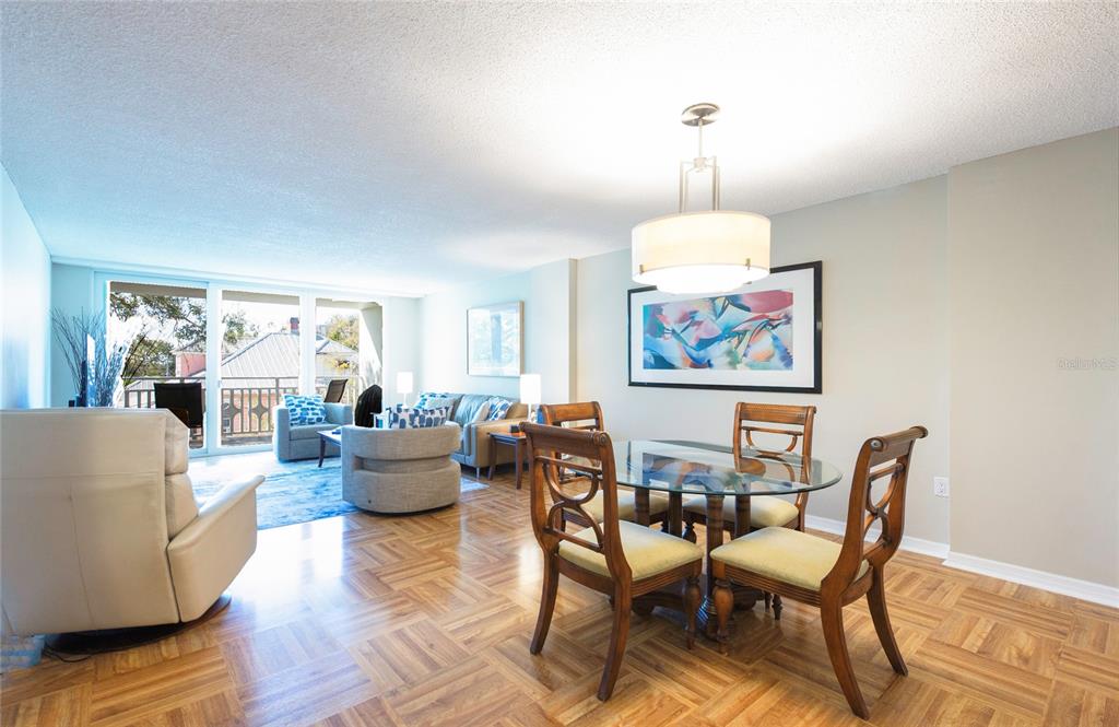 A dining area with a glass table and wooden chairs sits beside a living room — 700 BEACH DRIVE NE UNIT 406, ST PETERSBURG, FL