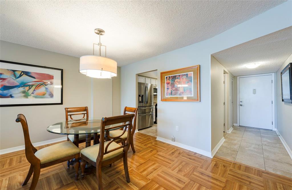 A dining area with a glass table, wooden chairs, and parquet flooring leads to a kitchen — 700 BEACH DRIVE NE UNIT 406, ST PETERSBURG, FL