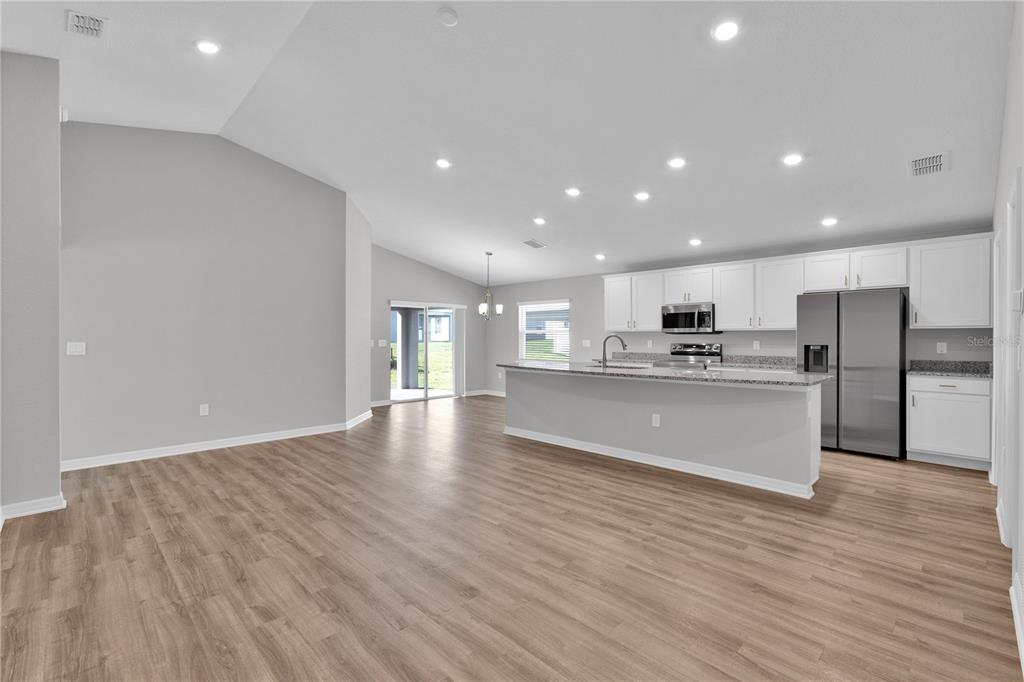 An open-concept kitchen and living area with light wood-look flooring and white cabinetry — 1823 BRISBANE PLACE, DAVENPORT, FL