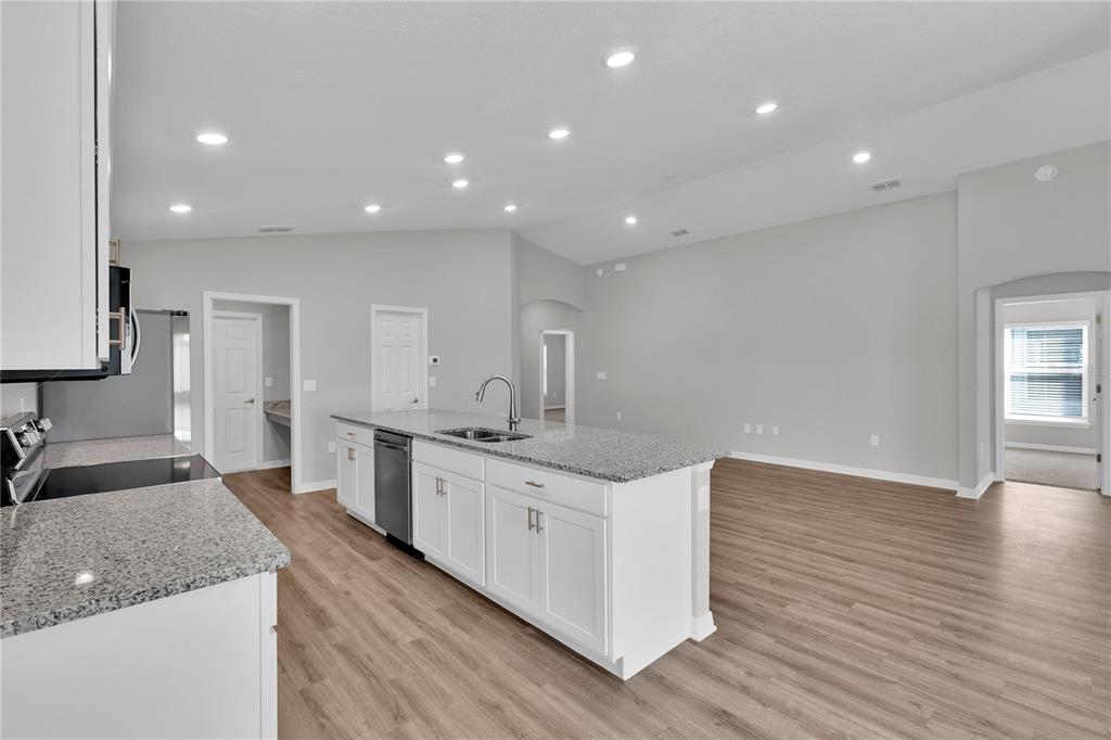 A kitchen with a granite-topped island and white cabinets opens into a spacious living area — 1823 BRISBANE PLACE, DAVENPORT, FL