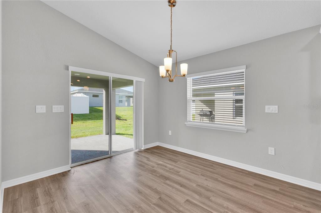 A dining area features light gray walls, wood-look flooring, a chandelier, and a sliding glass door — 1823 BRISBANE PLACE, DAVENPORT, FL