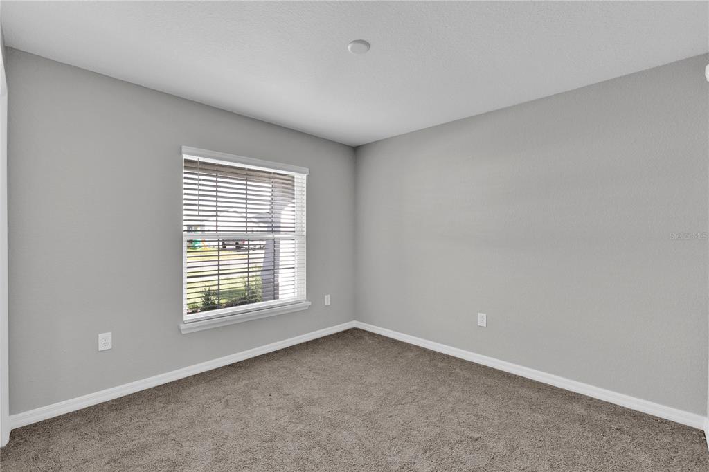 An empty bedroom features gray walls, beige carpet, and a window with white blinds — 1823 BRISBANE PLACE, DAVENPORT, FL