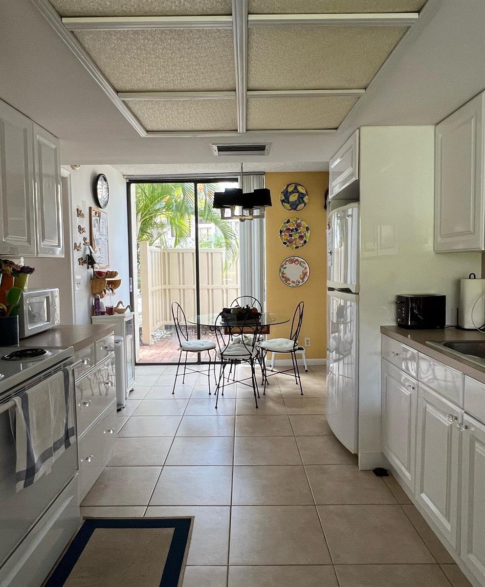 A galley-style kitchen with white cabinets, tile floors, and a dining area overlooking a patio — 1002 Bridgewood Place # 1002, Boca Raton FL 33434, BOCA RATON, FL