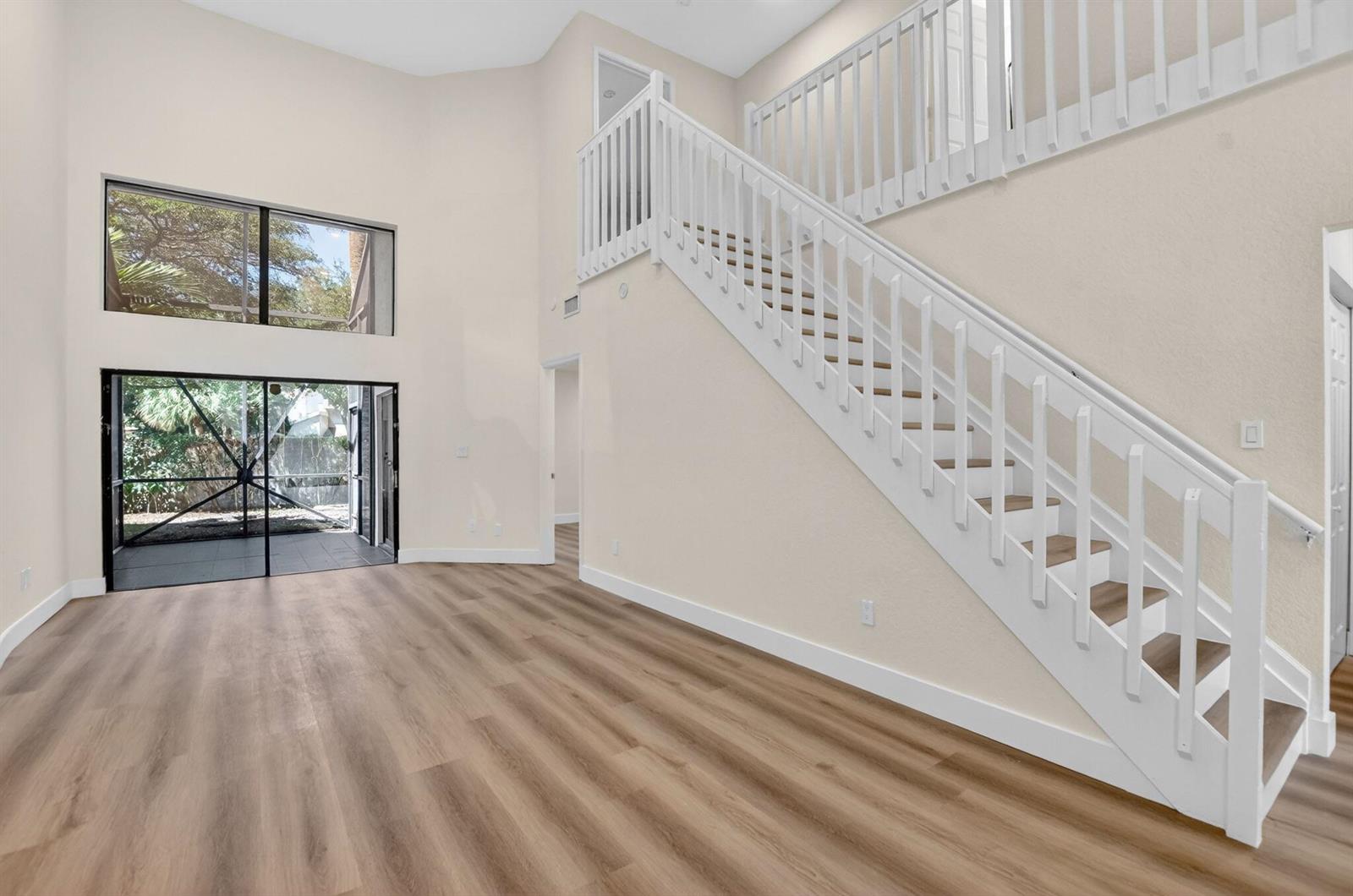 A living room with high ceilings, wood-look flooring, a staircase, and sliding glass patio doors — 6647 Boca Hermosa Lane, Boca Raton FL 33433, BOCA RATON, FL