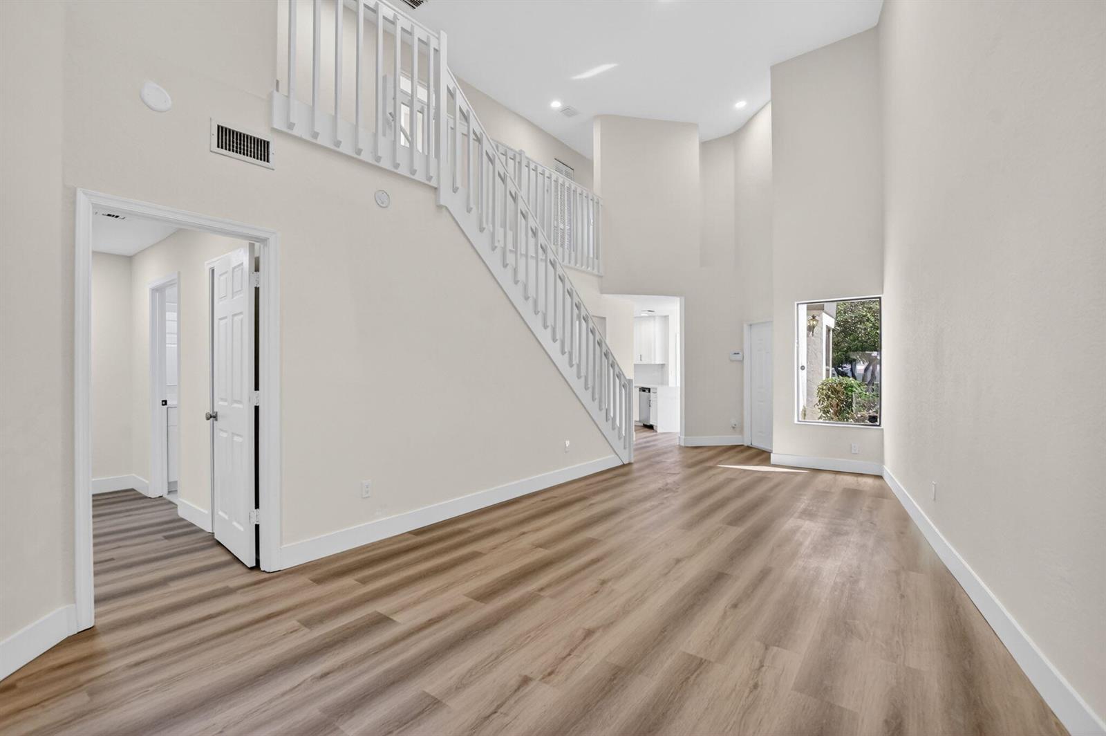 An empty room with light wood-look flooring, a white staircase, and high ceilings — 6647 Boca Hermosa Lane, Boca Raton FL 33433, BOCA RATON, FL