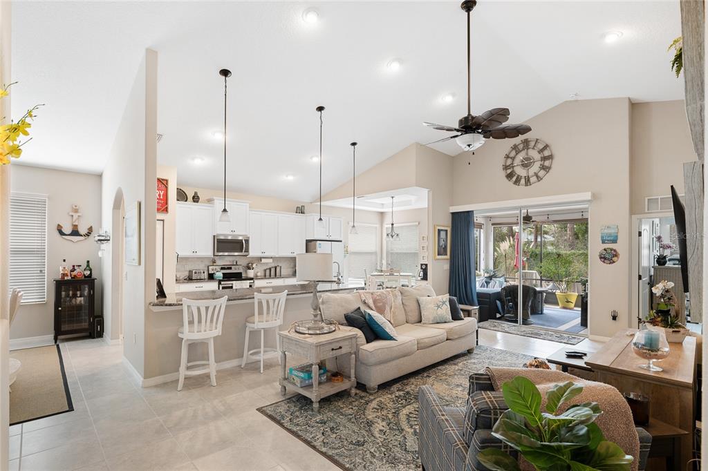 A bright open-concept living room features a kitchen with white cabinets and a vaulted ceiling — 107 PARK PLACE CIRCLE, PALM COAST, FL