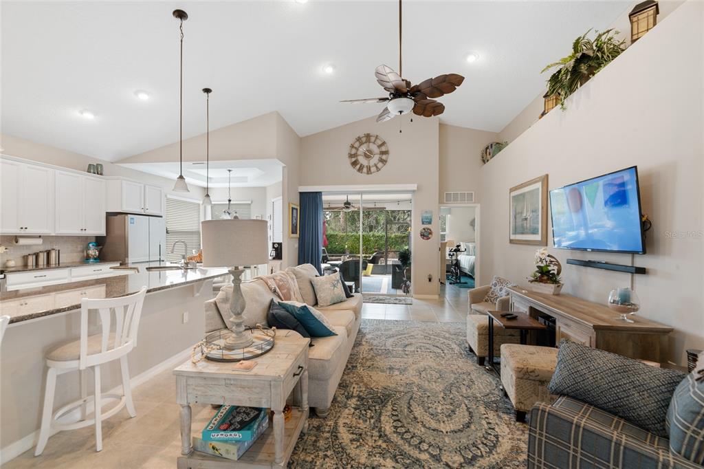 A living room with a vaulted ceiling, ceiling fan, and open kitchen with bar seating — 107 PARK PLACE CIRCLE, PALM COAST, FL