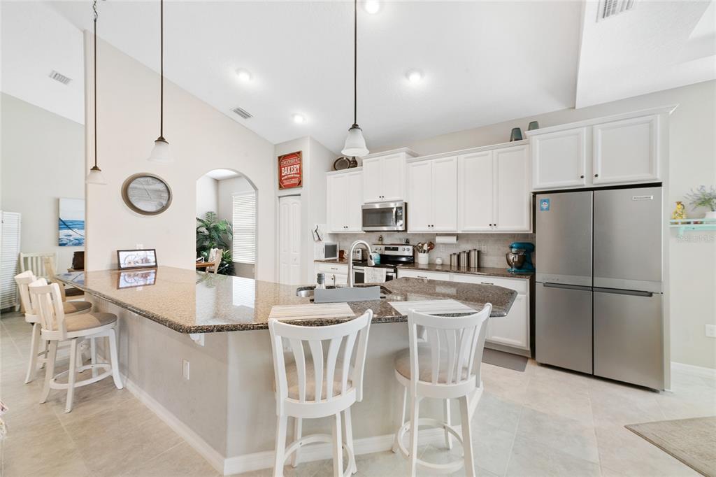 A kitchen features white cabinetry, granite countertops, a stainless steel refrigerator, and a breakfast bar — 107 PARK PLACE CIRCLE, PALM COAST, FL