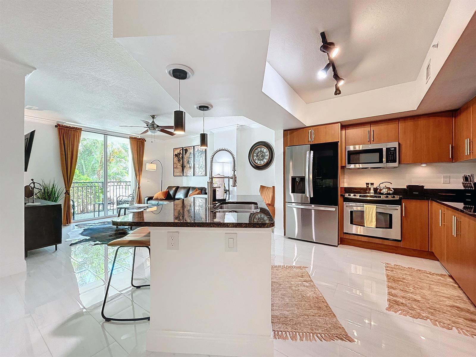 A kitchen with wood cabinets and a white island opens into a living area — 600 S Dixie Highway # 630, West Palm Beach FL 33401, WEST PALM BEACH, FL