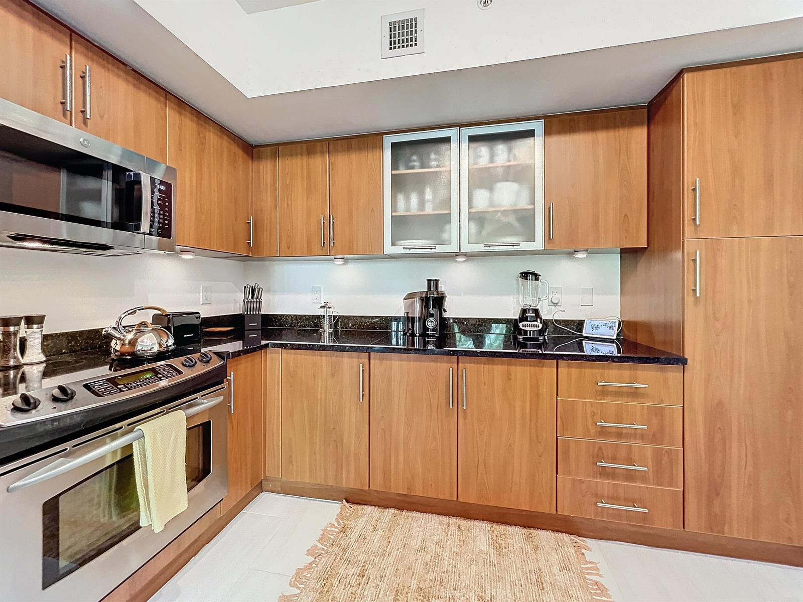 A kitchen features wood cabinets, dark granite countertops, stainless steel appliances, and a light rug — 600 S Dixie Highway # 630, West Palm Beach FL 33401, WEST PALM BEACH, FL