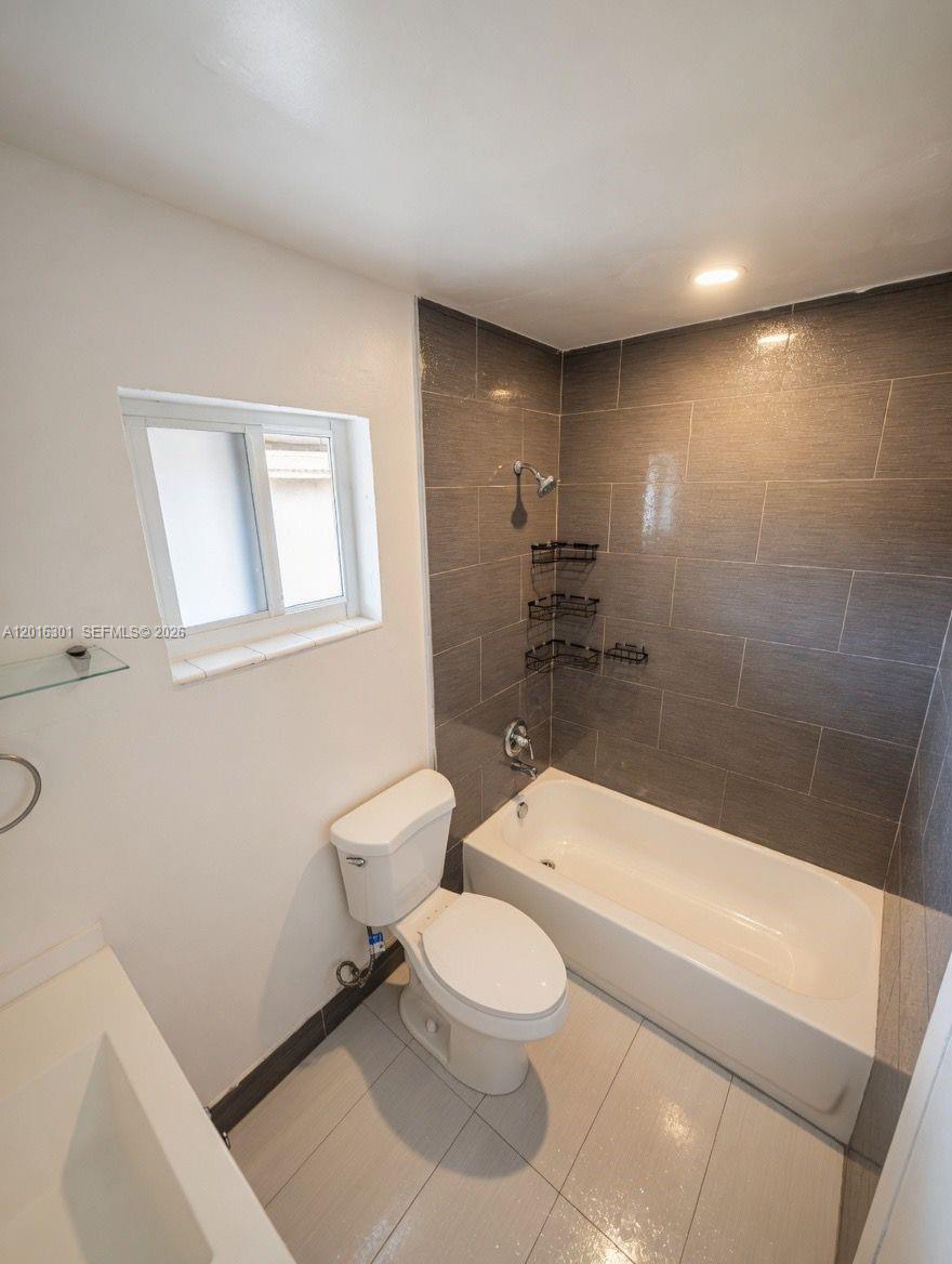A bathroom features a white toilet, a bathtub with gray tiled walls, and a window — 6850 W 14th Ct # C28, Hialeah FL 33014, HIALEAH, FL