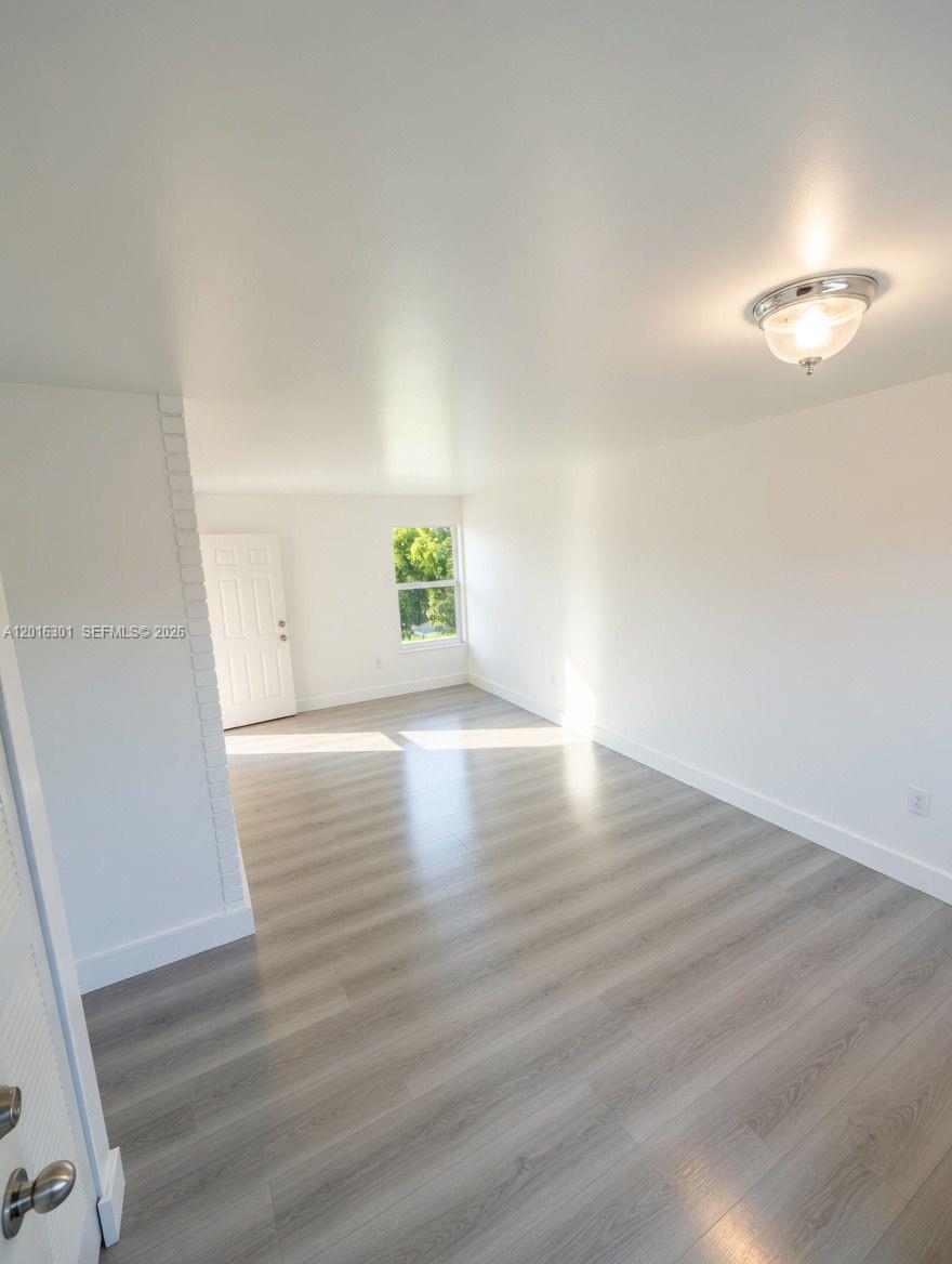 An empty room features light-colored wood-look flooring, white walls, and a single window — 6850 W 14th Ct # C28, Hialeah FL 33014, HIALEAH, FL