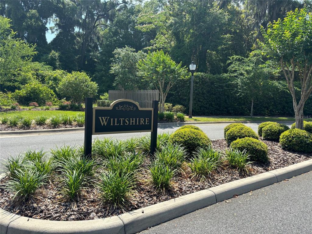A sign reading Wiltshire stands in a landscaped garden bed near a paved road — 2148 NW 50TH WAY, GAINESVILLE, FL