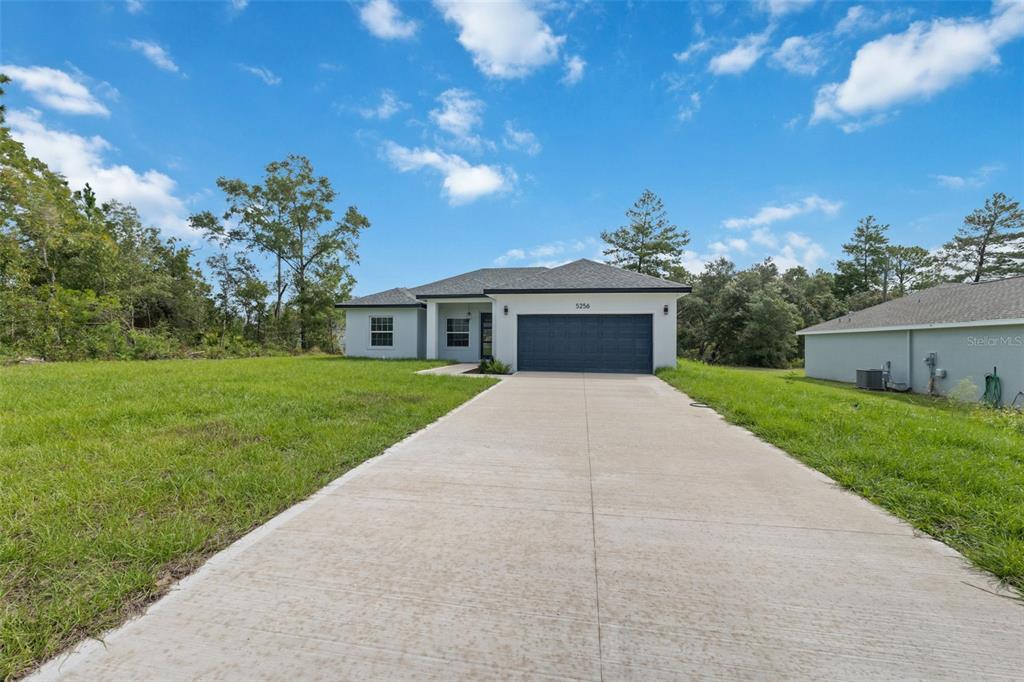 A single-story house with a concrete driveway and a dark garage door sits on grass — 5256 SW 155TH LOOP, OCALA, FL